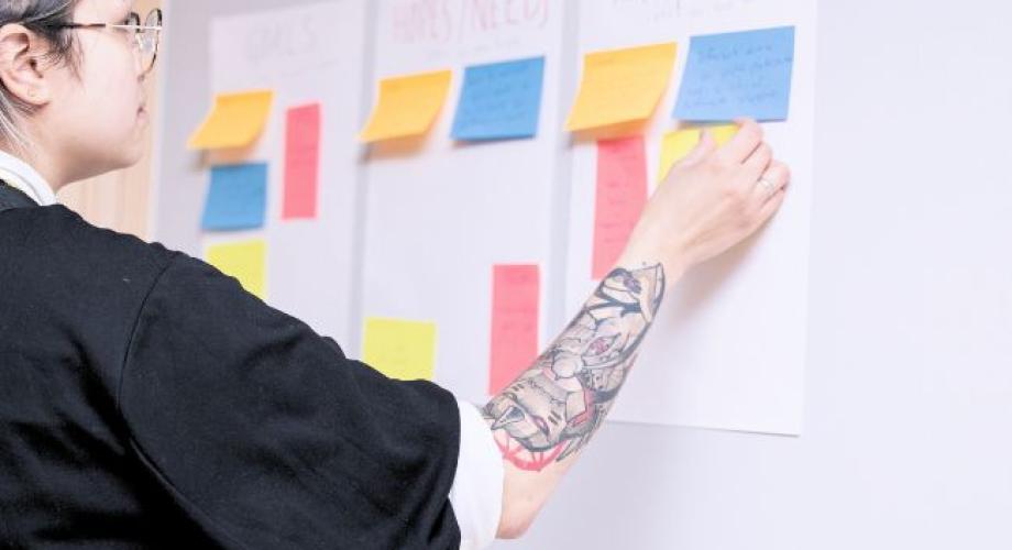 Henkilö liimaa post it -lappuja seinälle.