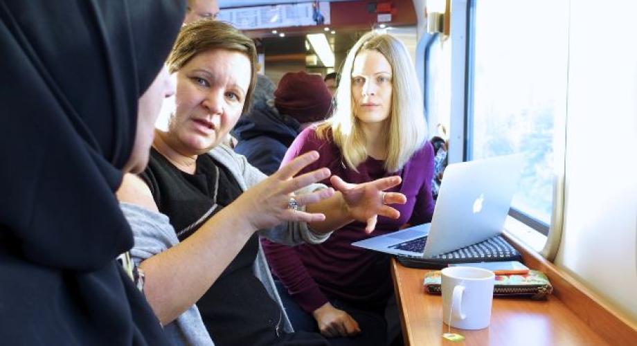 Kolme henkilöä keskustelee kannettavan tietokoneen äärellä junassa.