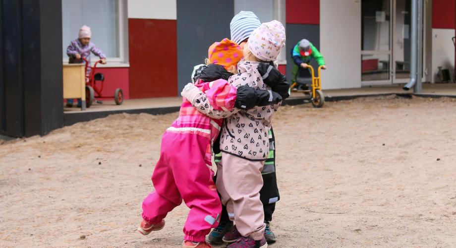 Joukko päiväkoti-ikäisiä lapsia halaavat toisiaan ulkona.