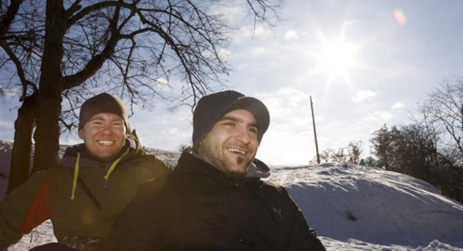 Kaksi miestä laskemassa pulkalla mäkeä aurinkoisessa säässä