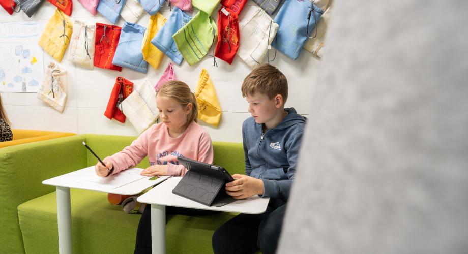 Kaksi oppilasta työskentelee luokassa tabletin ja vihkon äärellä