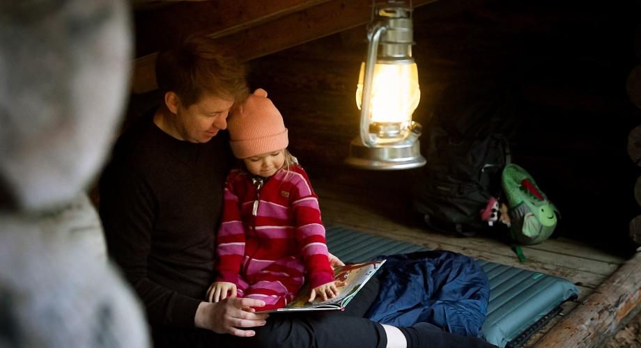 Isä ja lapsi lukevat kirjaa laavulla.