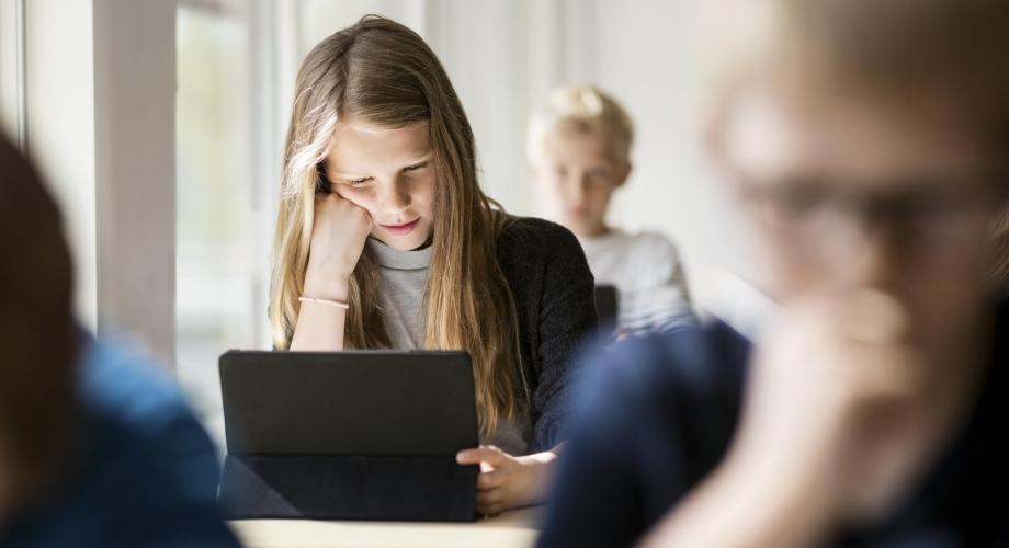 Opiskelija katsoo tablet-tietokonetta luokassa.