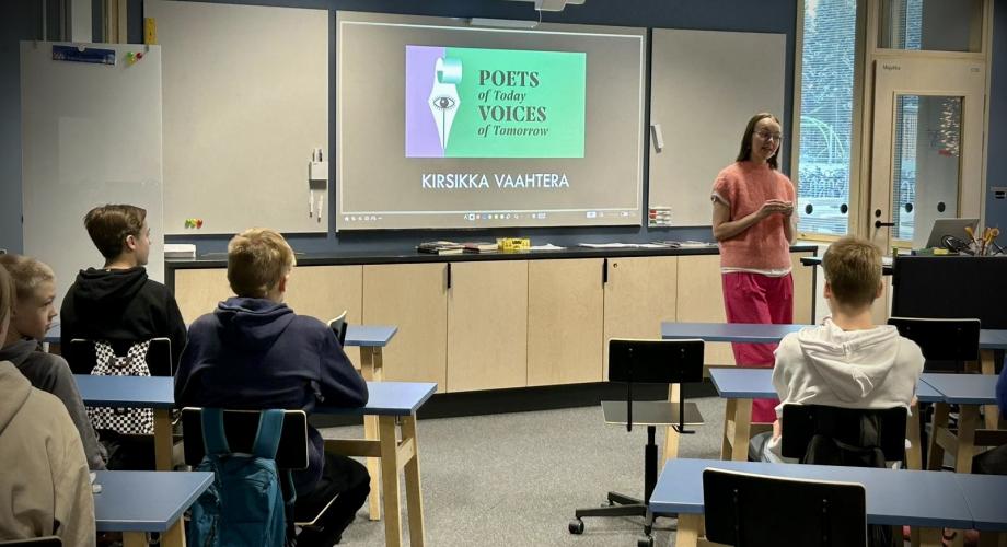Värikkäästi pukeutunut runoilija kertoo koululuokalle Poets of Today Voices of Tomorrow -hankkeesta