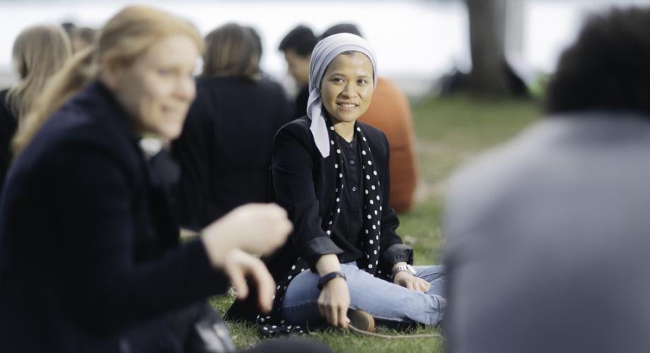 A woman is sitting on the lawn of a university campus in spring.