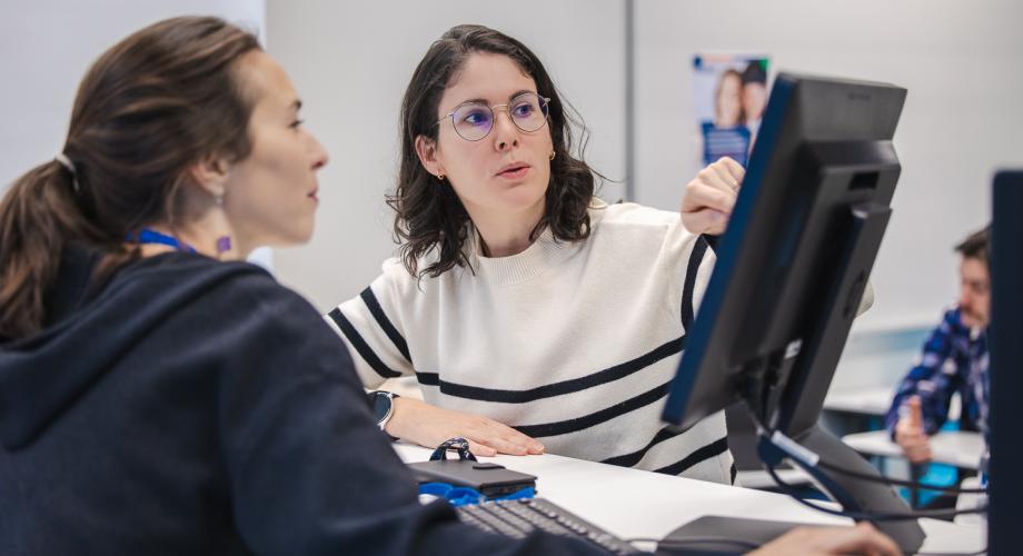 Two women are looking at a computer screen in a classroom.