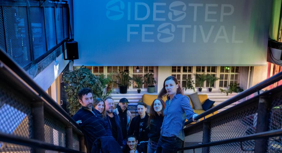 Kuvassa joukko ihmisiä portaikossa ja heidän takanaan teksti Sidestep Festival