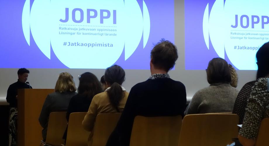 Tilassa istuu ihmisiä kuuntelemassa seminaaria.