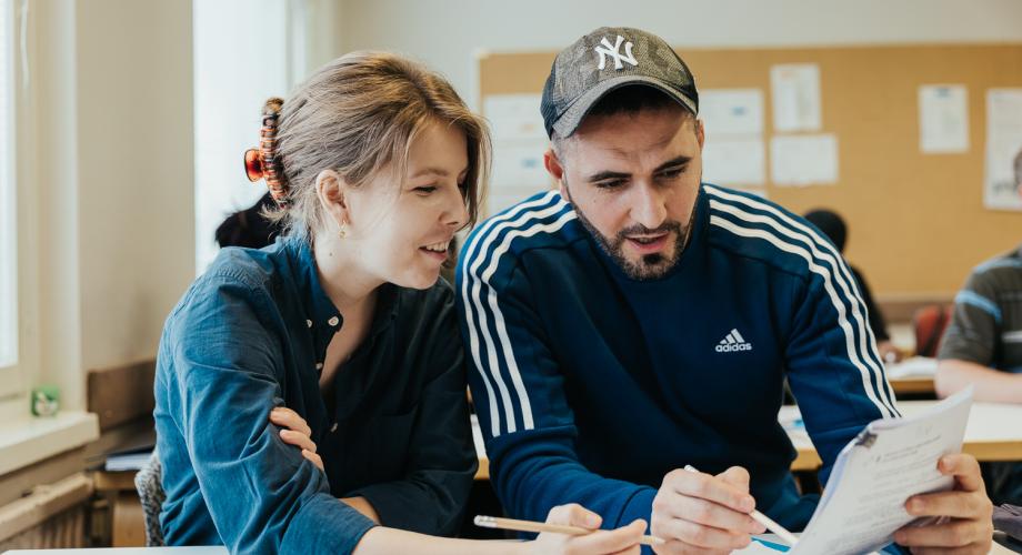 Kaksi henkilöä tutkii opiskelutehtävää luokkahuoneessa. 