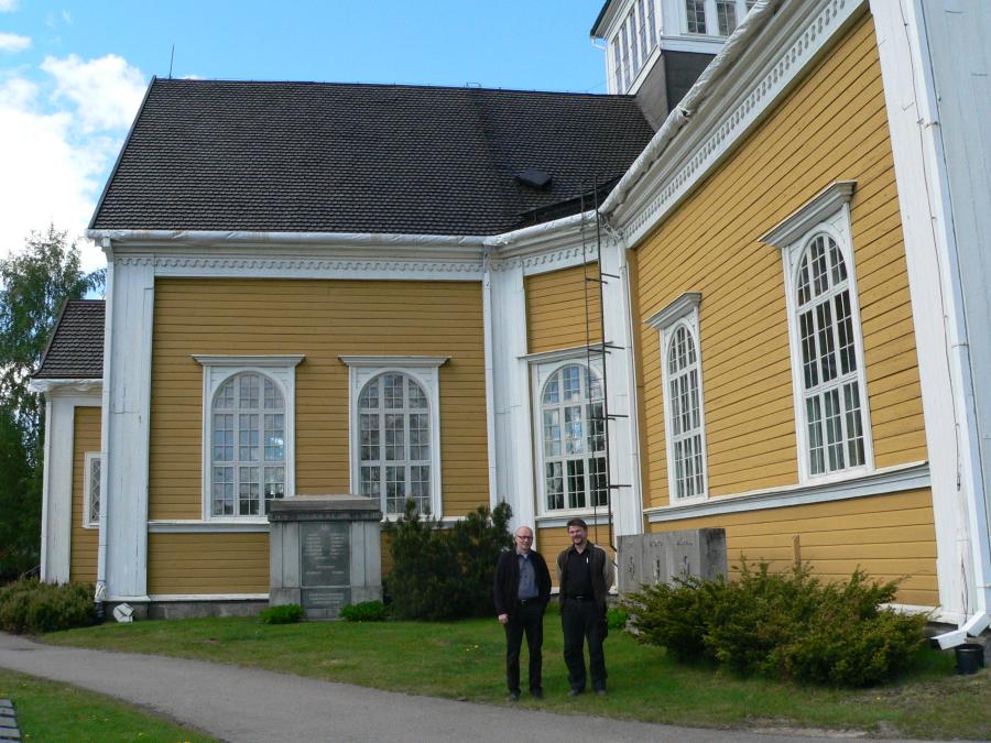 Ikaalisten käsi- ja taideteollisuusoppilaitoksen opettajat Heikki Jylhä-Vuorio ja Esko Huhtala Ikaalisten kirkon edustalla. Kirkon katon tervaaminen perinteiseen tapaan oli osa rakennusentisöinnin opiskelijoiden opintoja.