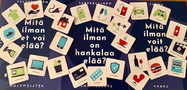 Välttämätön, tarpeellinen, turha -korttipelin kansikuvassa vilahtaa yksinkertaisesti piirrettyjä kortteja kolmesta osiosta: välttämättömästä, tarpeellisesta ja turhasta. Välttämättömässä osiossa lukee valkoisella fontilla: Mitä ilman et voi elää. Tarpeellisen osiossa lukee valkoisella fontilla: Mitä ilman on hankala elää? Turhan osion kohdalla taas lukee valkoisella fontilla: Mitä ilman voit elää?