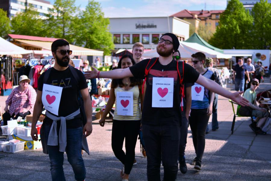 Joukko nuoria kävelee kadulla Ilmaisia haleja -kyltit kaulassaan.