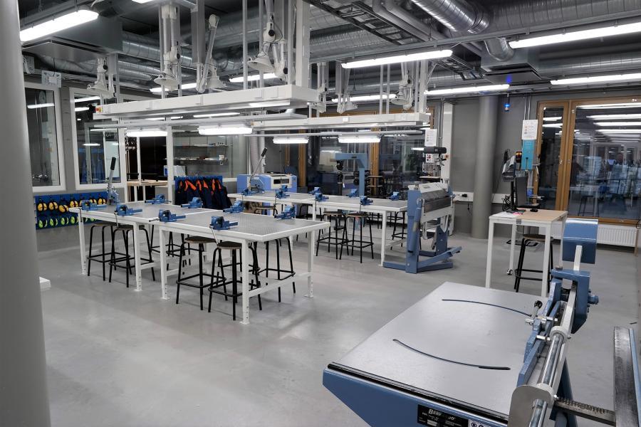 Kuvituskuva. Metallityötilassa sijaitsevat työpöydät, joissa usein paikat viilapenkeille. Lisäksi tilassa sijaitsee monia metallityöstöön liittyviä työvälineitä, kuten kaarisakset, levynpyöristin, kantintaivutin, pylväsporakoneet, sikkikone ja käsityövälineet.
