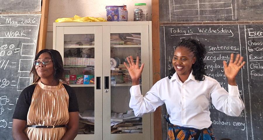 Two teachers in front of the blackboard in a sign language classroom in Zambia. The teacher on the right is using sign language to speak to her class.