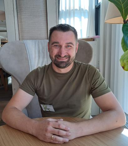 Man with dark hair and beard sitting at a desk smiling at the camera